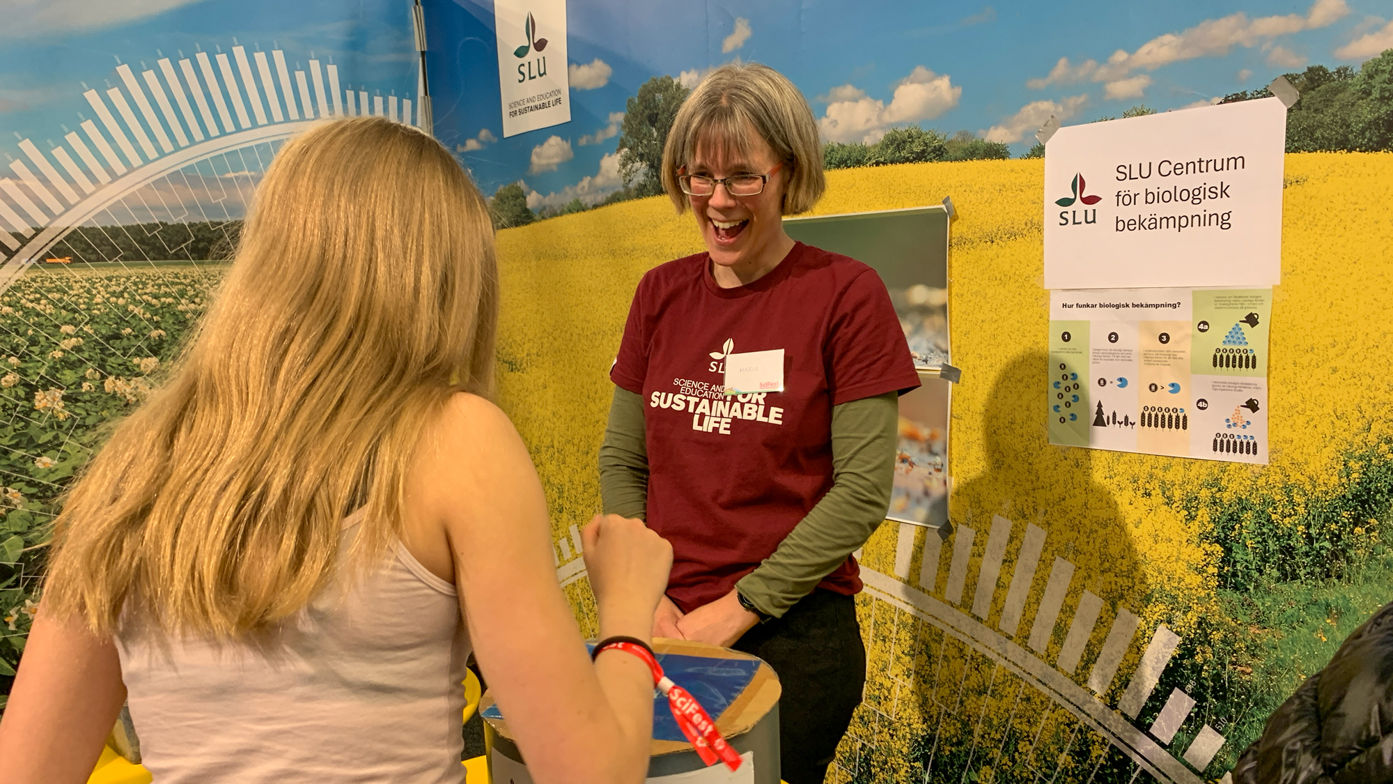 Ett barn sticker ner handen i en låda och en vuxen person skrattar. Foto.