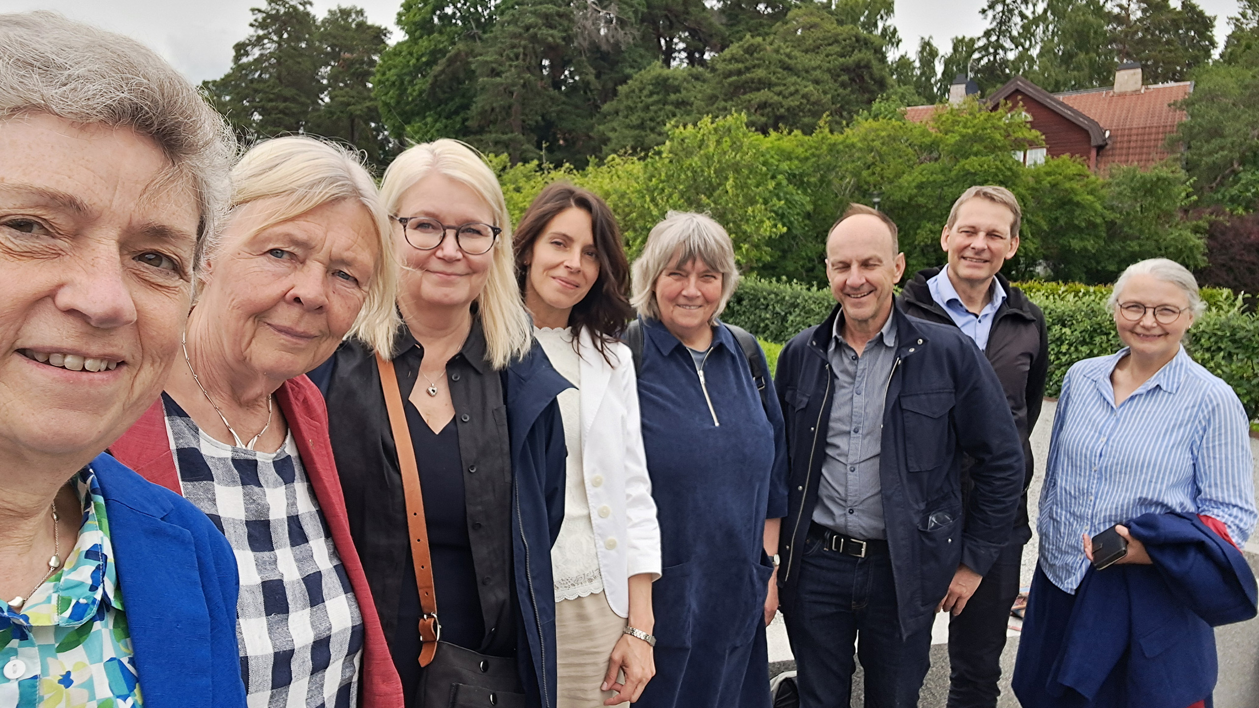 Åtta personer står på rad utomhus. Grönskande växtlighet i bakgrunden.