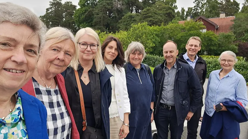 Åtta personer står på rad utomhus. Grönskande växtlighet i bakgrunden.