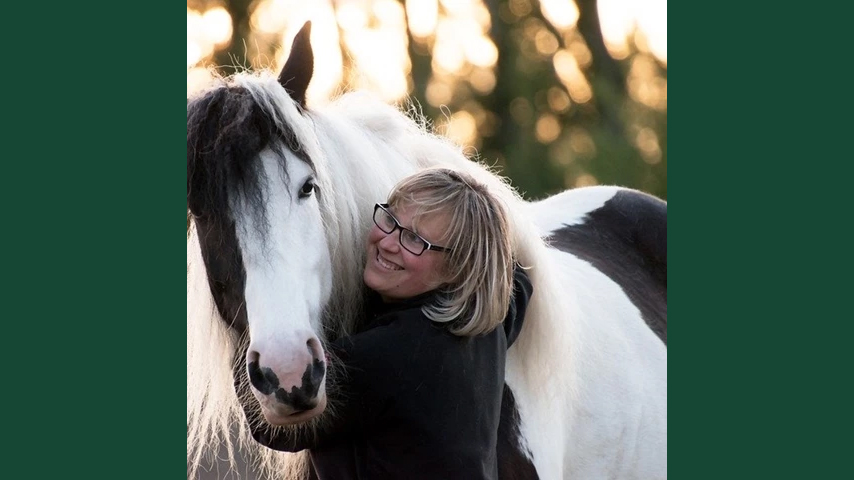 Foto av en kvinna som står med armarna om en stor hästs hals.
