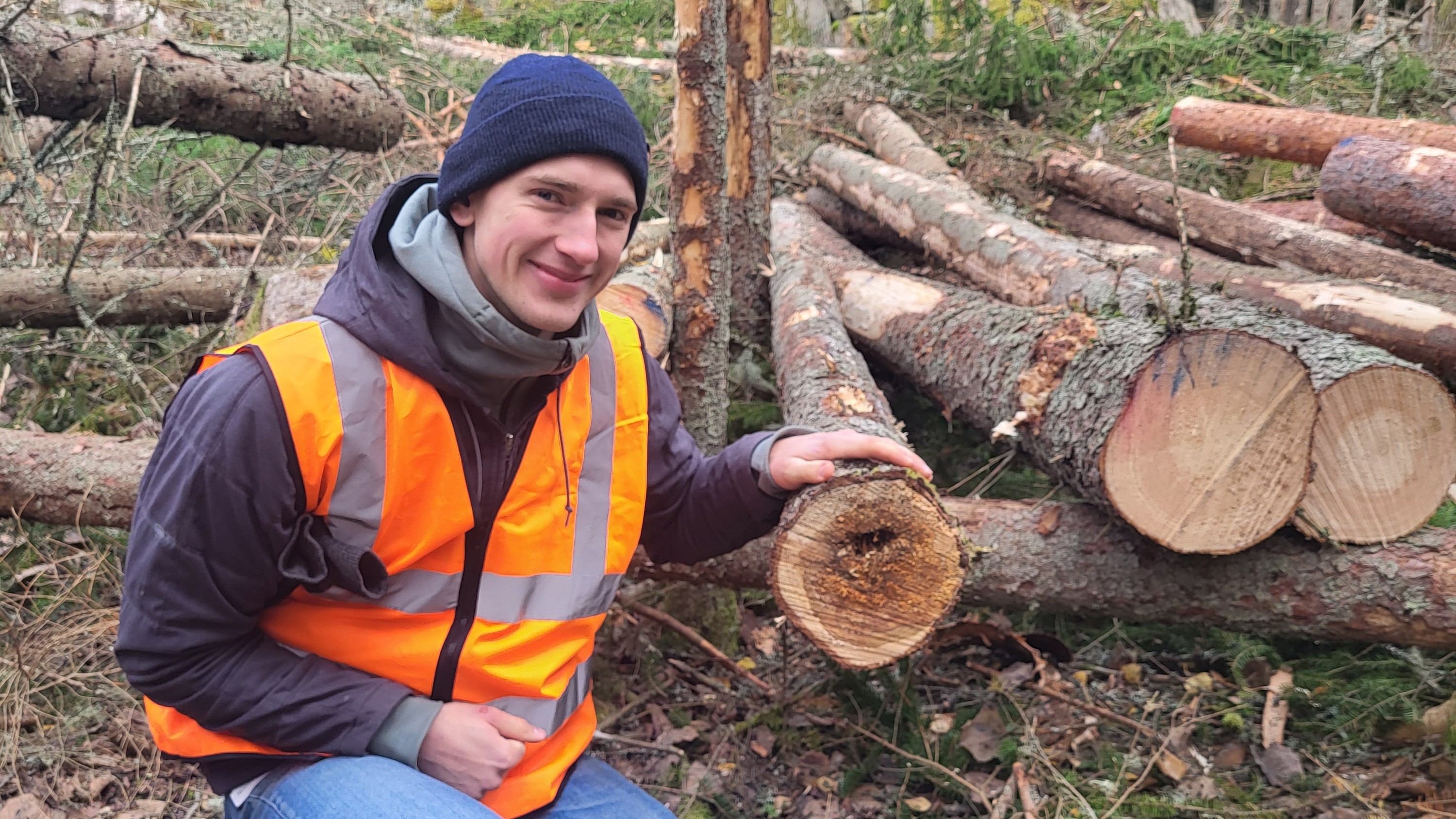 Doktorand Isak bredvid rotrötat träd. Foto. 