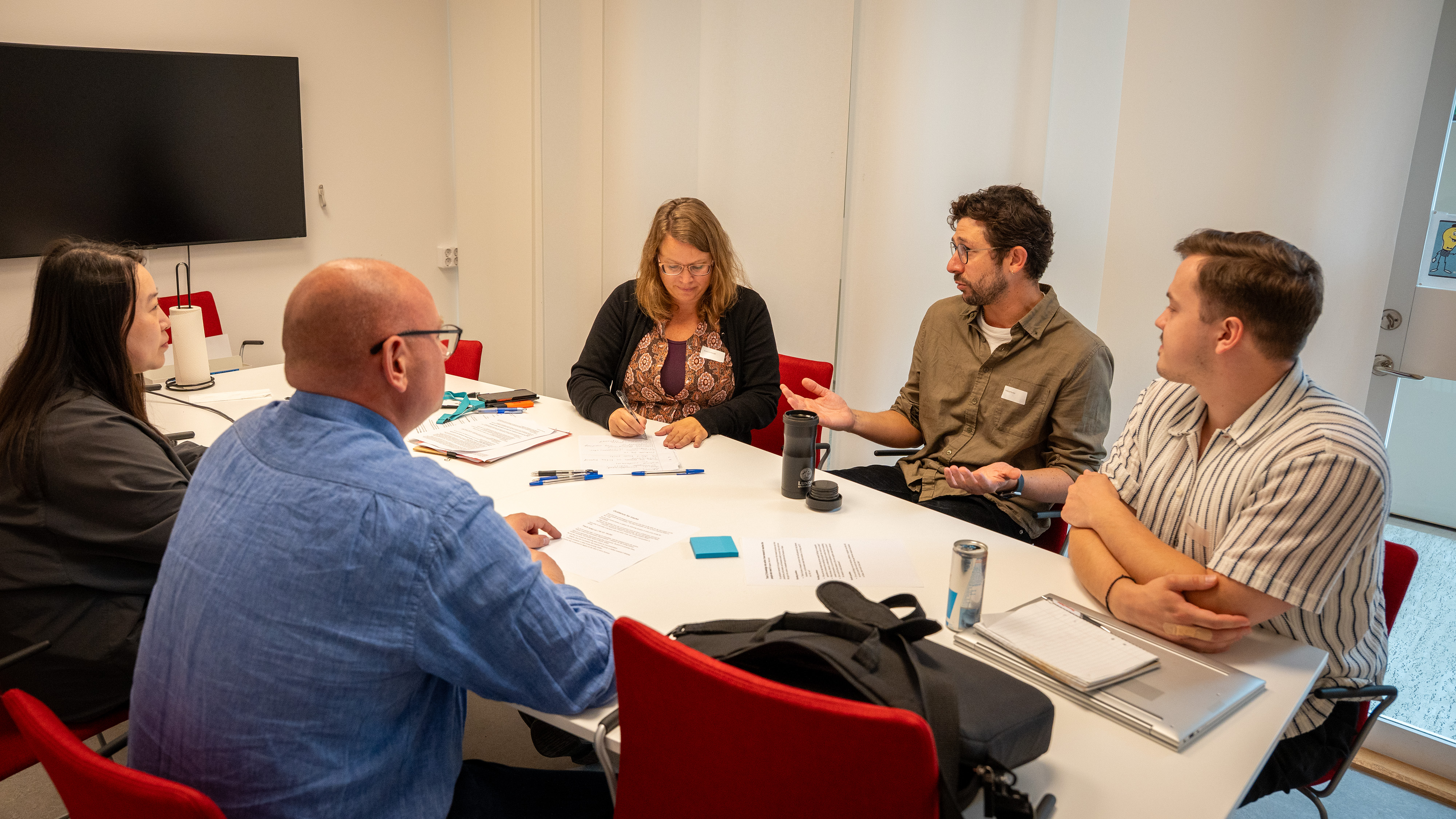 Five people is sitting around a table, talking.