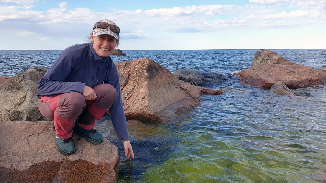 A smiling woman on a rock reaching her hand towards the water. Photo.