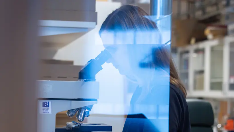 Photo of a woman (Emma Thilén, SLU) sitting at a microscope in a laboratory.