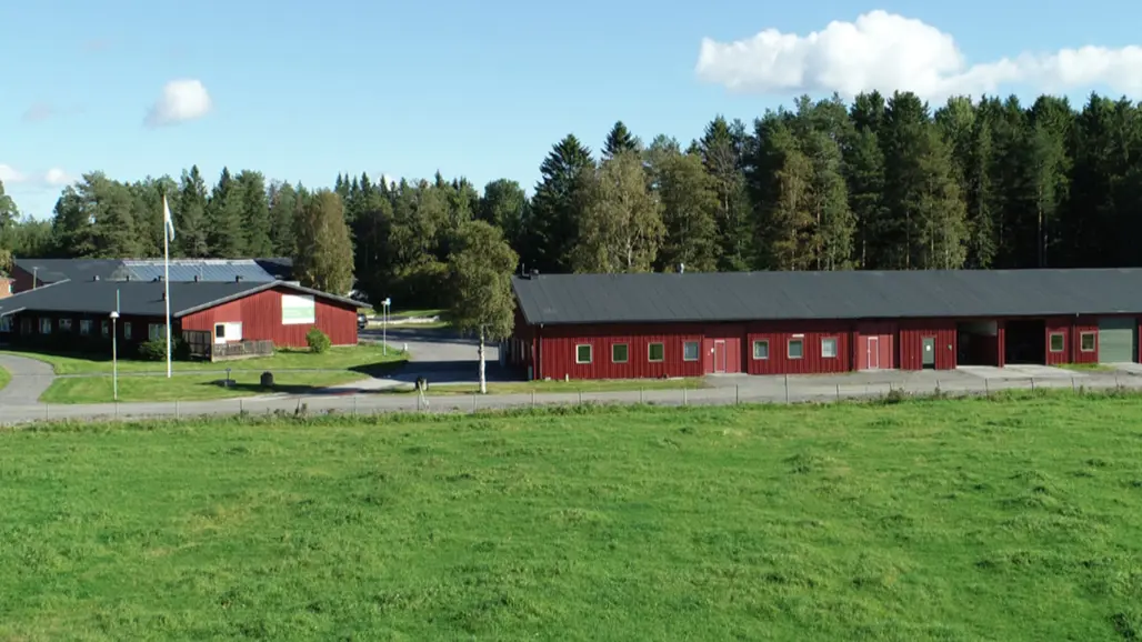 Två röda byggnader längs en väg och skog i bakgrunden.