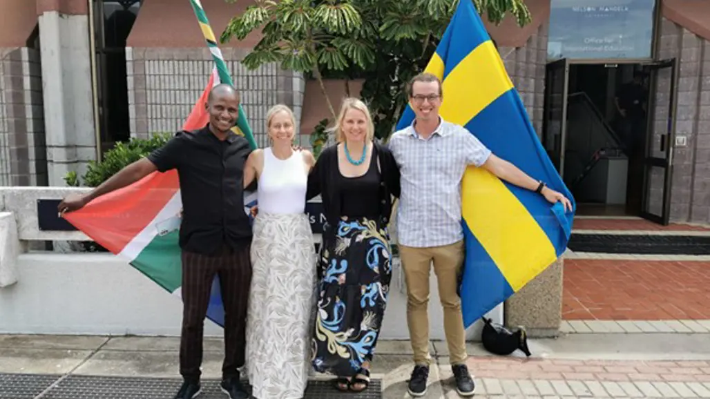 Four happy researchers from South Africa and Sweden pose together with their national flags outside Nelson Mandela University