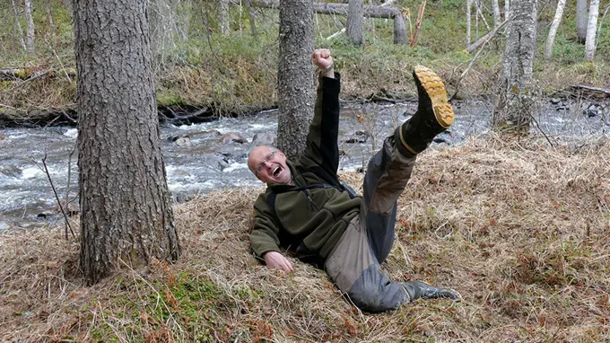 Lycklig man ligger i skog och gestikulerar med ben och armar. Foto