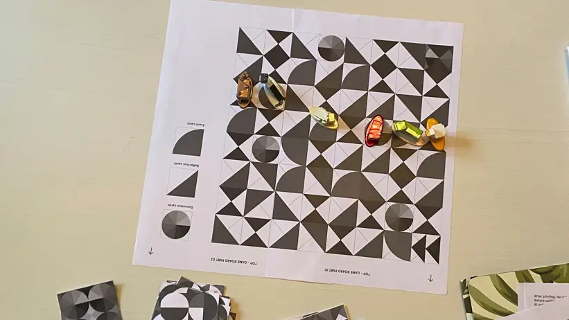 A printed black and white game board with six game pieces. Photo.