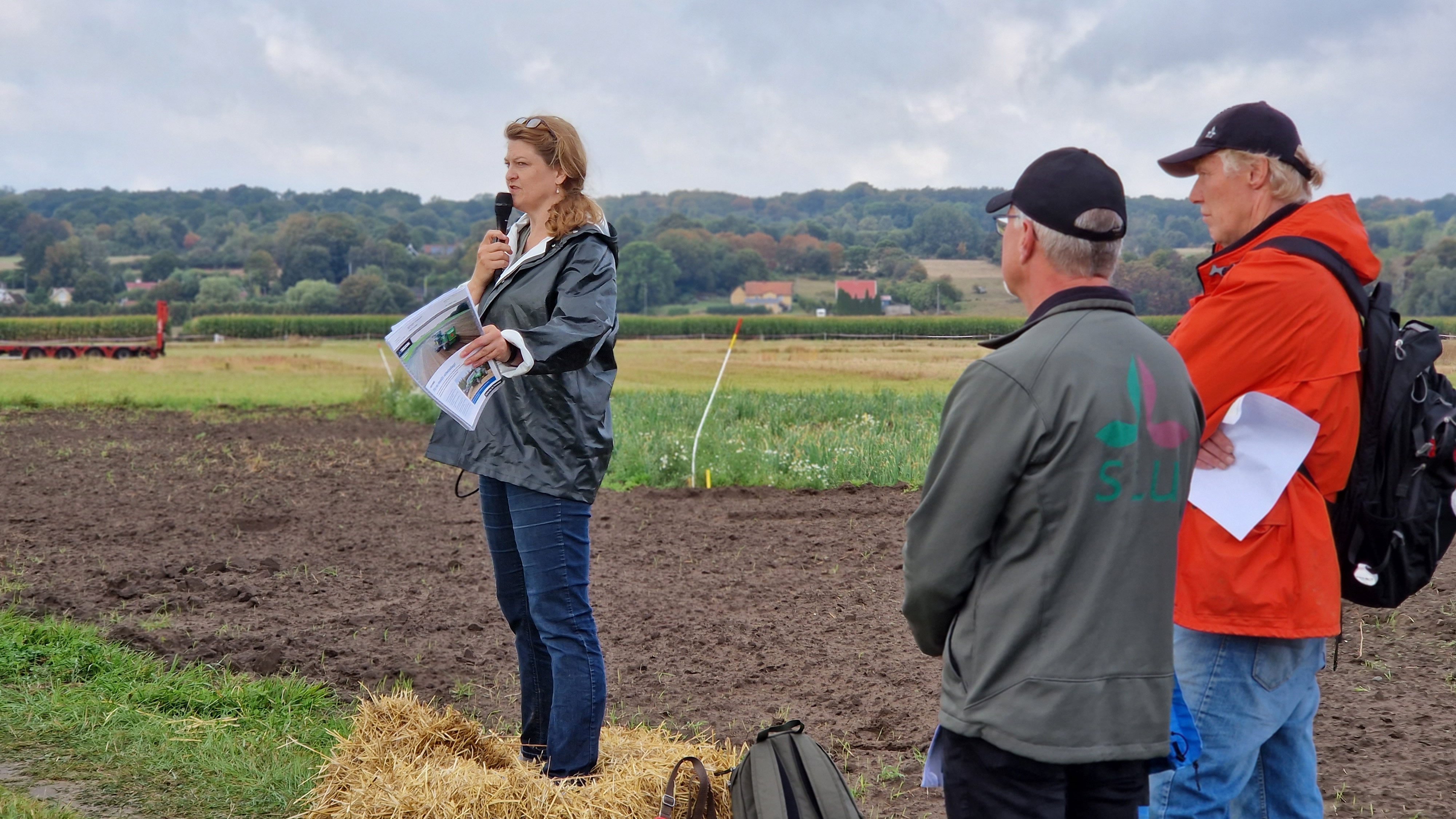 En kvinna håller en fältpresentation. I förgrunden syns två män med profilkläder från SLU.