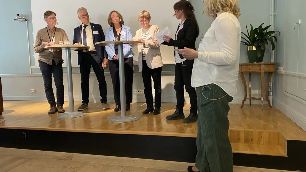 En grupp människor står uppradade och diskuterar vid några ståbord. Foto.
