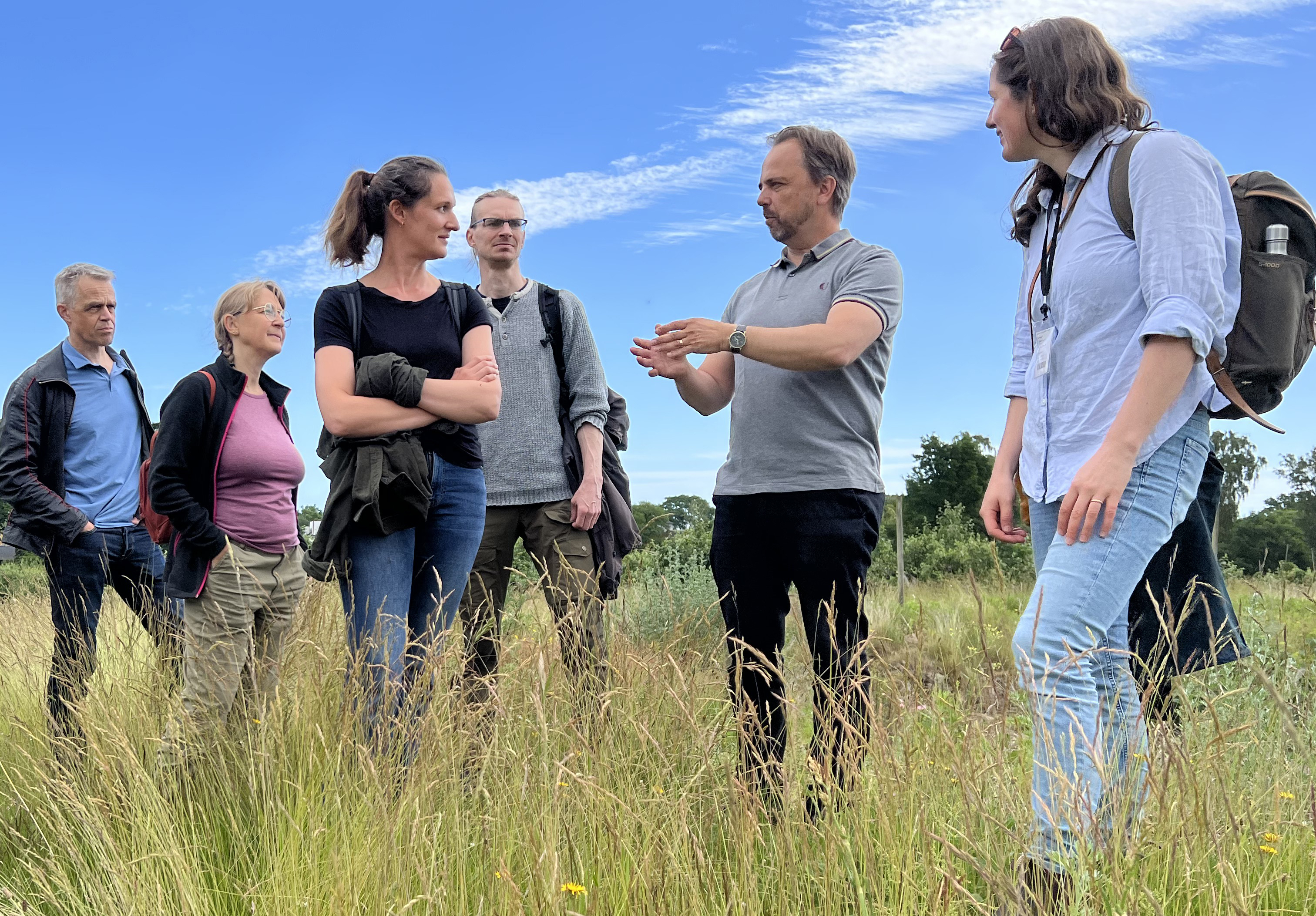 Grupp människor som står och samtalar på en äng