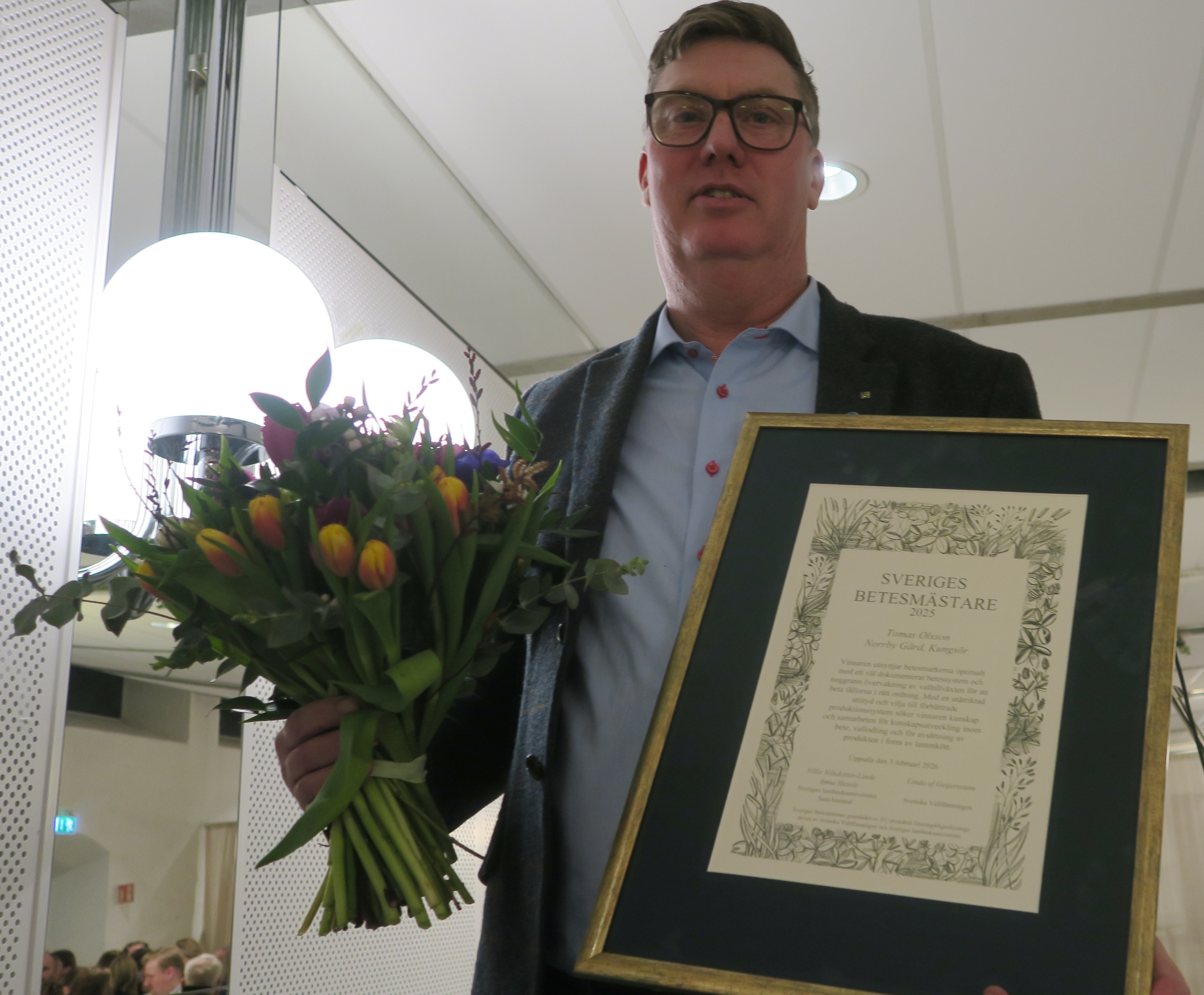 Thomas Olsson håller ett inramat diplom och en stor blombukett. Foto.