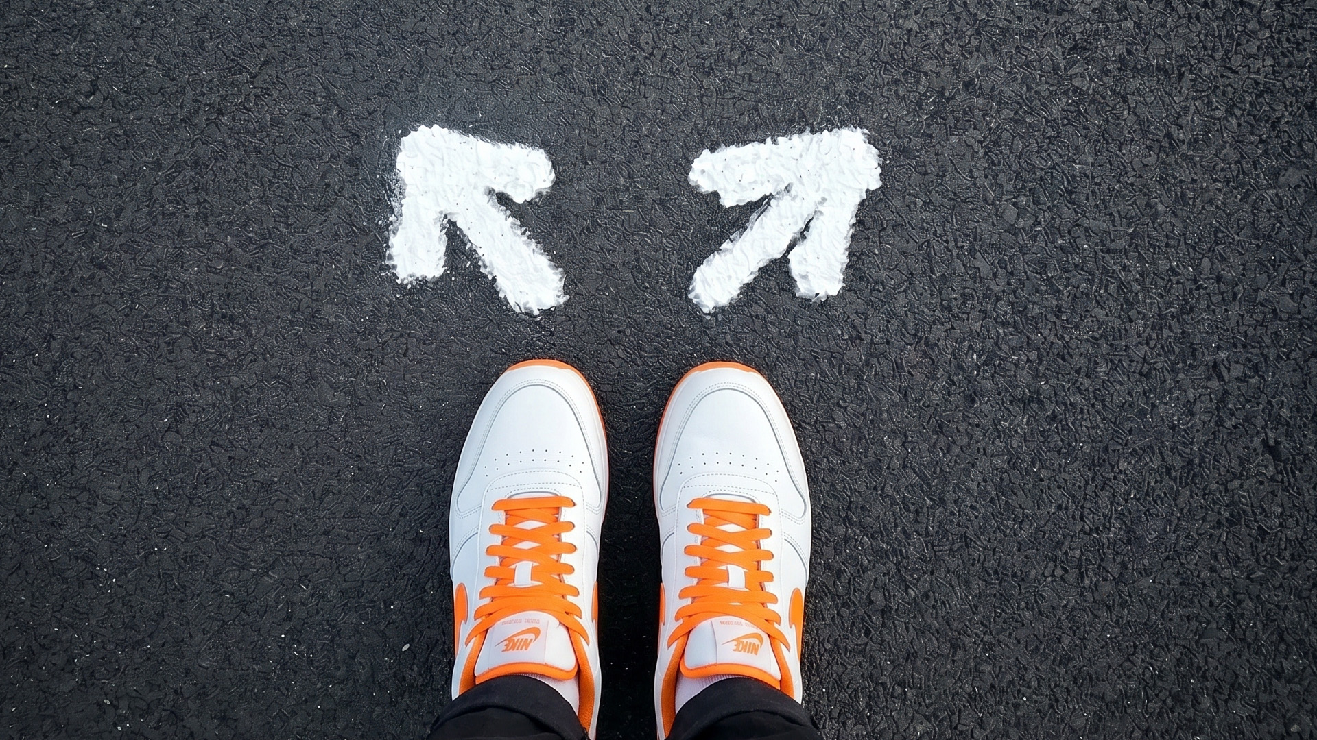 Vita sneakers med orange snören. På asfalten framför skorna pekar två vita pilar åt varsitt håll. Ai-genererat foto.
