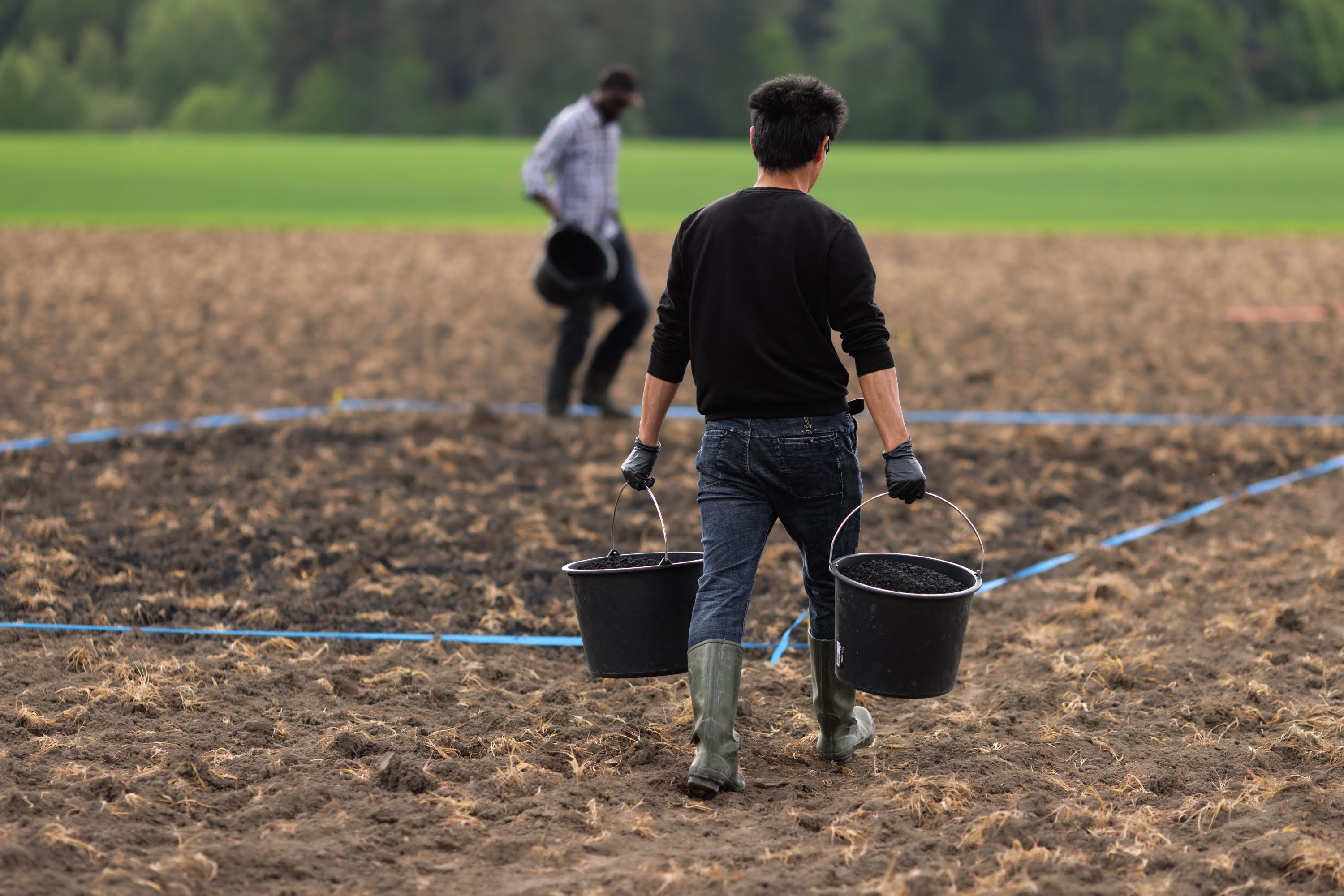 A red tractor transports an orange bag in an arable field