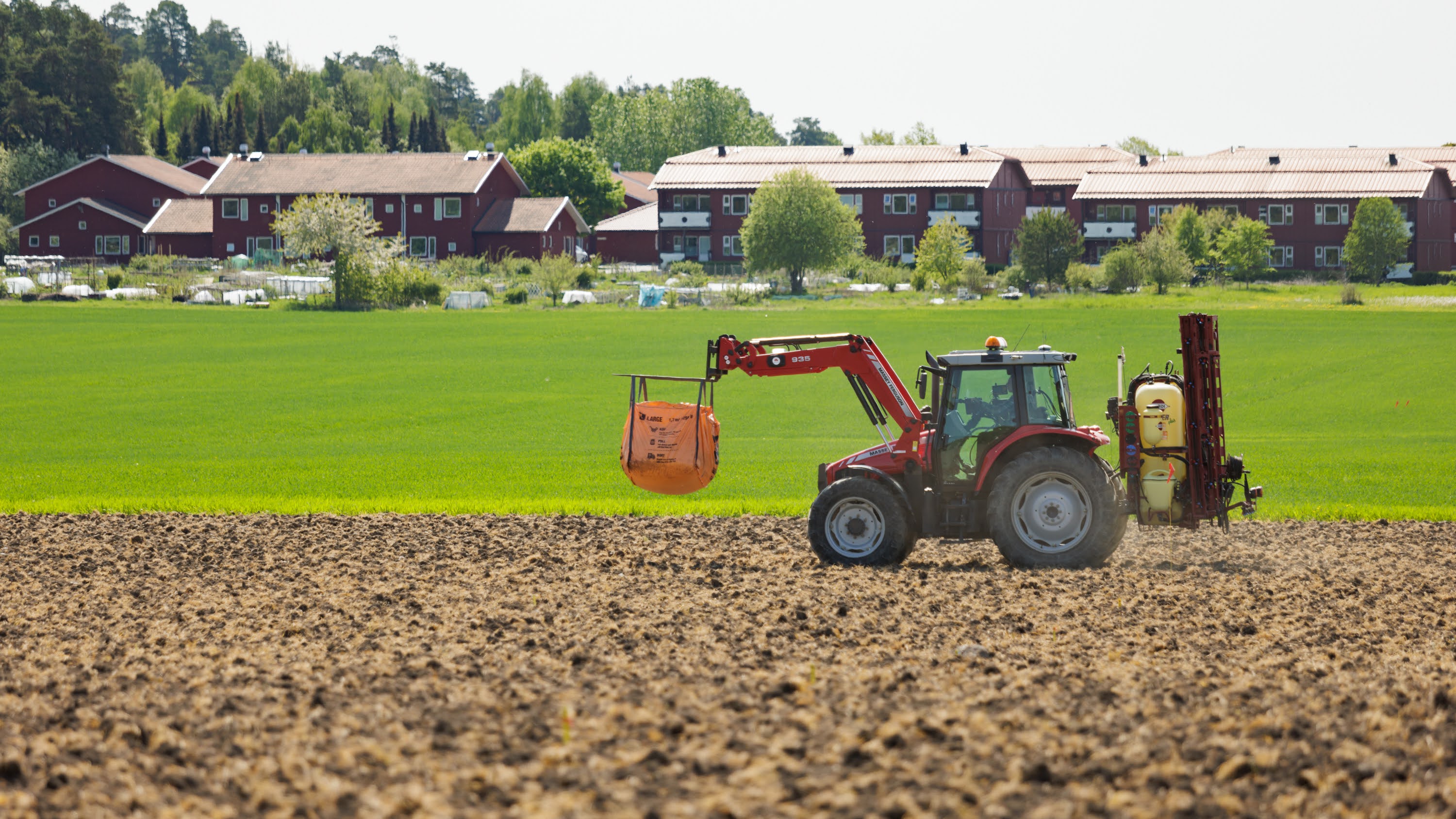 A red tractor transports an orange bag in an arable field
