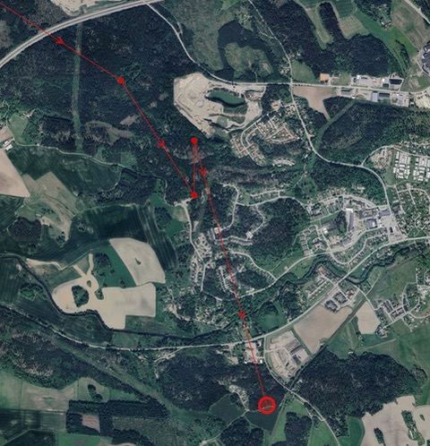 Satellitbild som visar ett landskap med skog, åkrar och bostadsområden. Röda linjer och punkter markerar en rutt eller väg genom området, med synliga vägar och byggnader.  Foto.