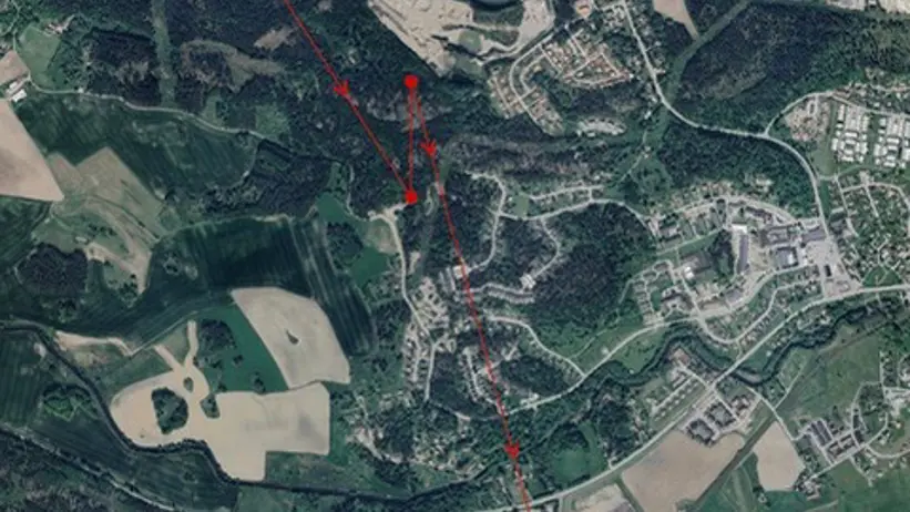 Satellitbild som visar ett landskap med skog, åkrar och bostadsområden. Röda linjer och punkter markerar en rutt eller väg genom området, med synliga vägar och byggnader. Foto.