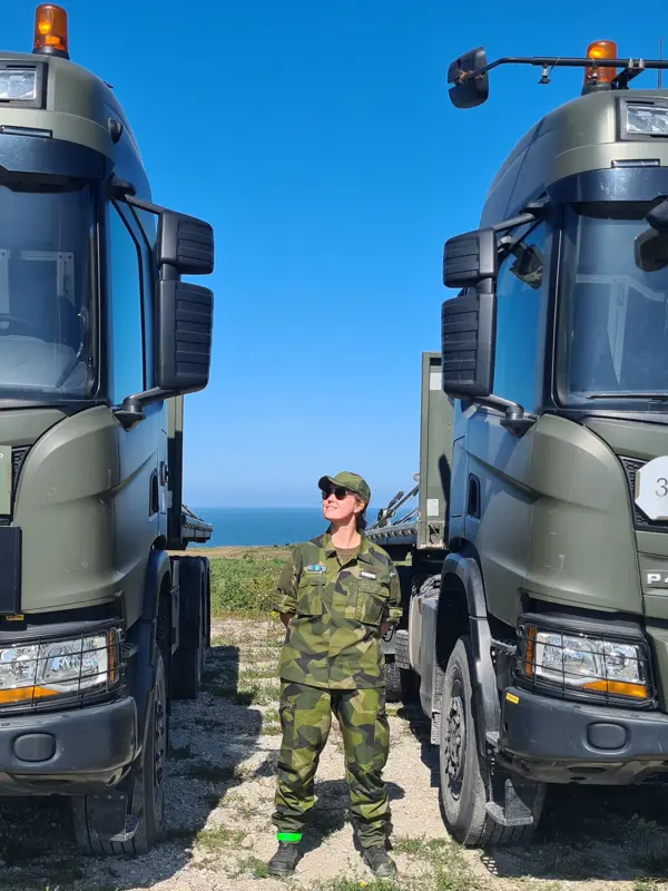 Kvinna i uniform mellan två tunga lastbilar