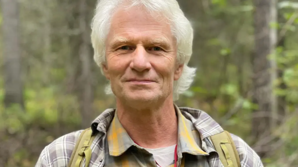 A person with white hair standing in the woods.
