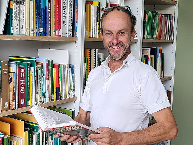 Andreas i ett bibliotek med en uppslagen bok i händerna. Foto.