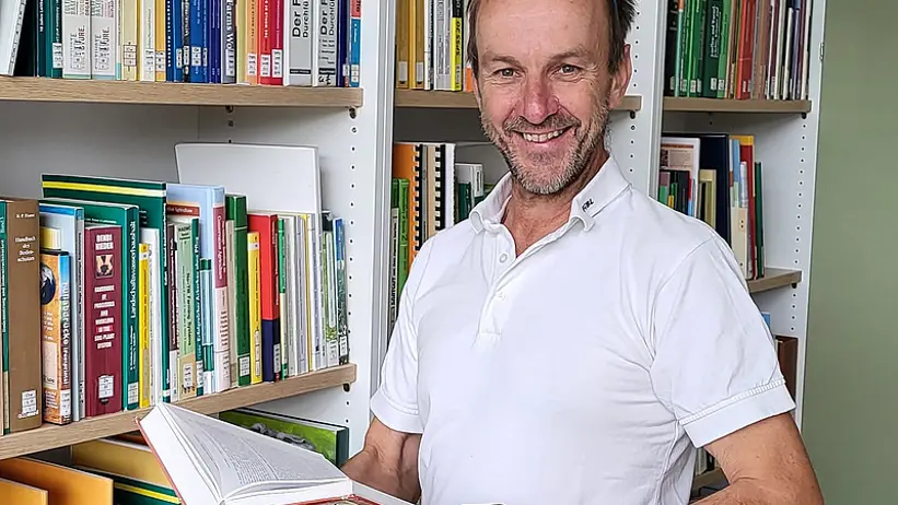 Andreas i ett bibliotek med en uppslagen bok i händerna. Foto.