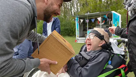 En utomhuspedagog låter ett barn i rullstol lukta i en låda med tång.