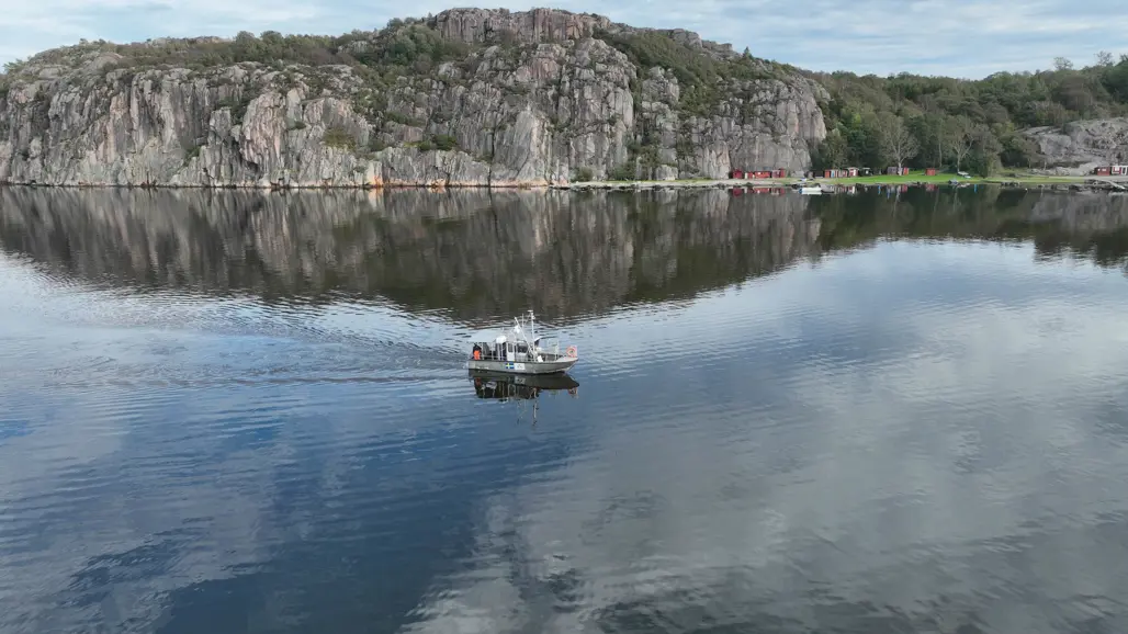 A beautiful coastal setting with a fishing boat in calm waters, surrounded by dramatic rock formations and some small buildings in the background.