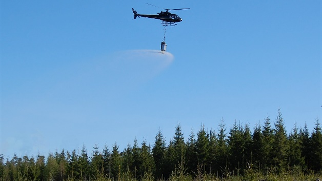 The image shows a helicopter that spreads fertilizers from the air
