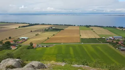 Ett landskap med fält och vatten i bakgrunden.