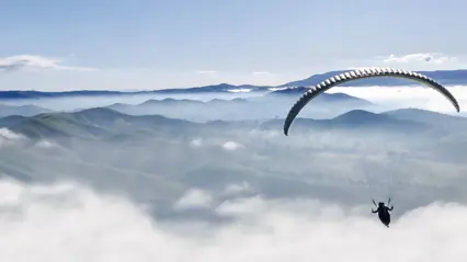 A paraglider over mountains and clouds. Photo: Shutterstock.