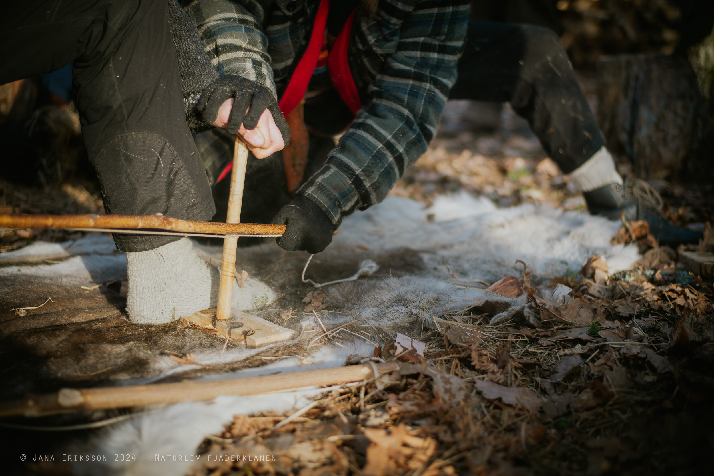 Två personer gör upp friktionseld med bågdrill
