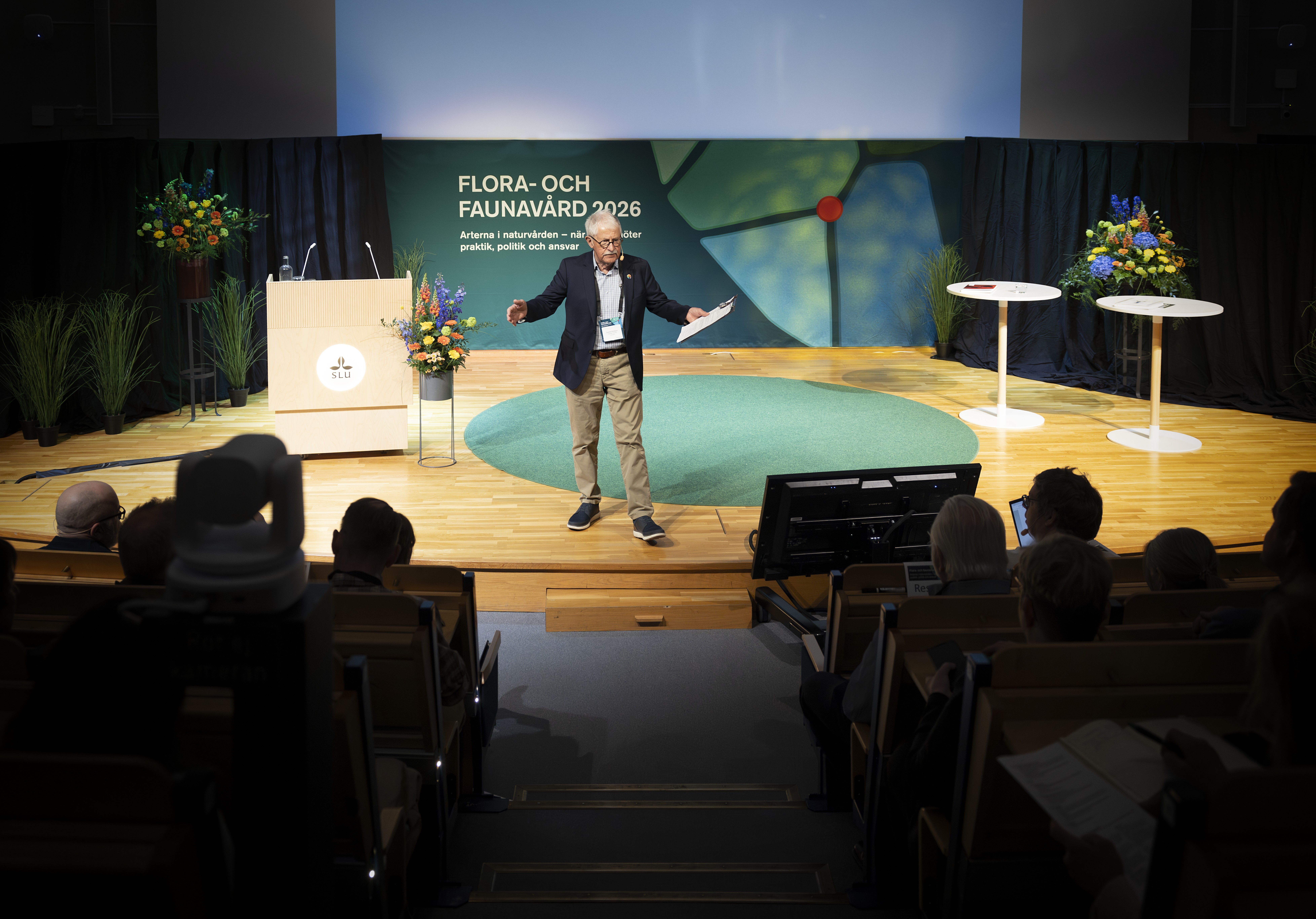 Man står på scen och hälsar välkommen till konferensen. Foto