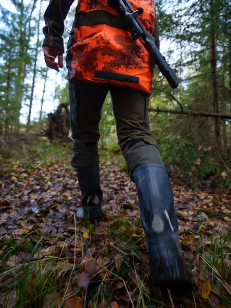 En jägarklädd person med ett gevär går i skogen. Foto.