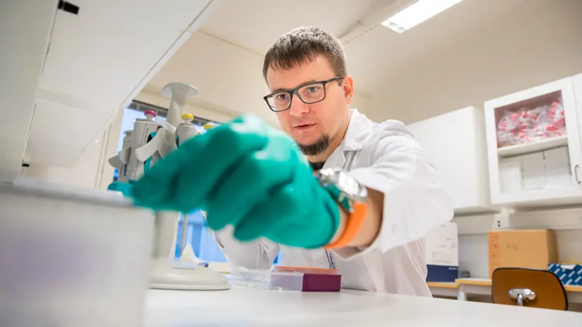 En man i labbrock och handskar är upptagen med att genomföra ett experiment vid en arbetsstation i ett laboratorium.