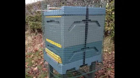 En bikupa täckt av ett plastnät. Rundstavar som handtag.