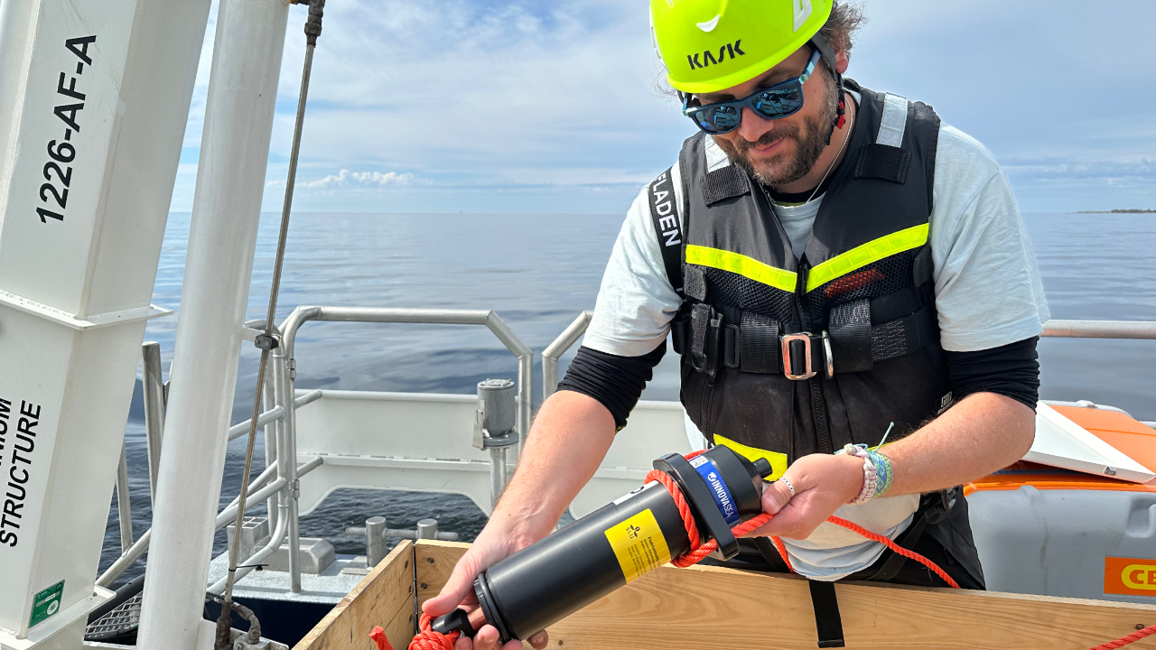 A person wearing a helmet is standing on a boat, holding a black receiver.