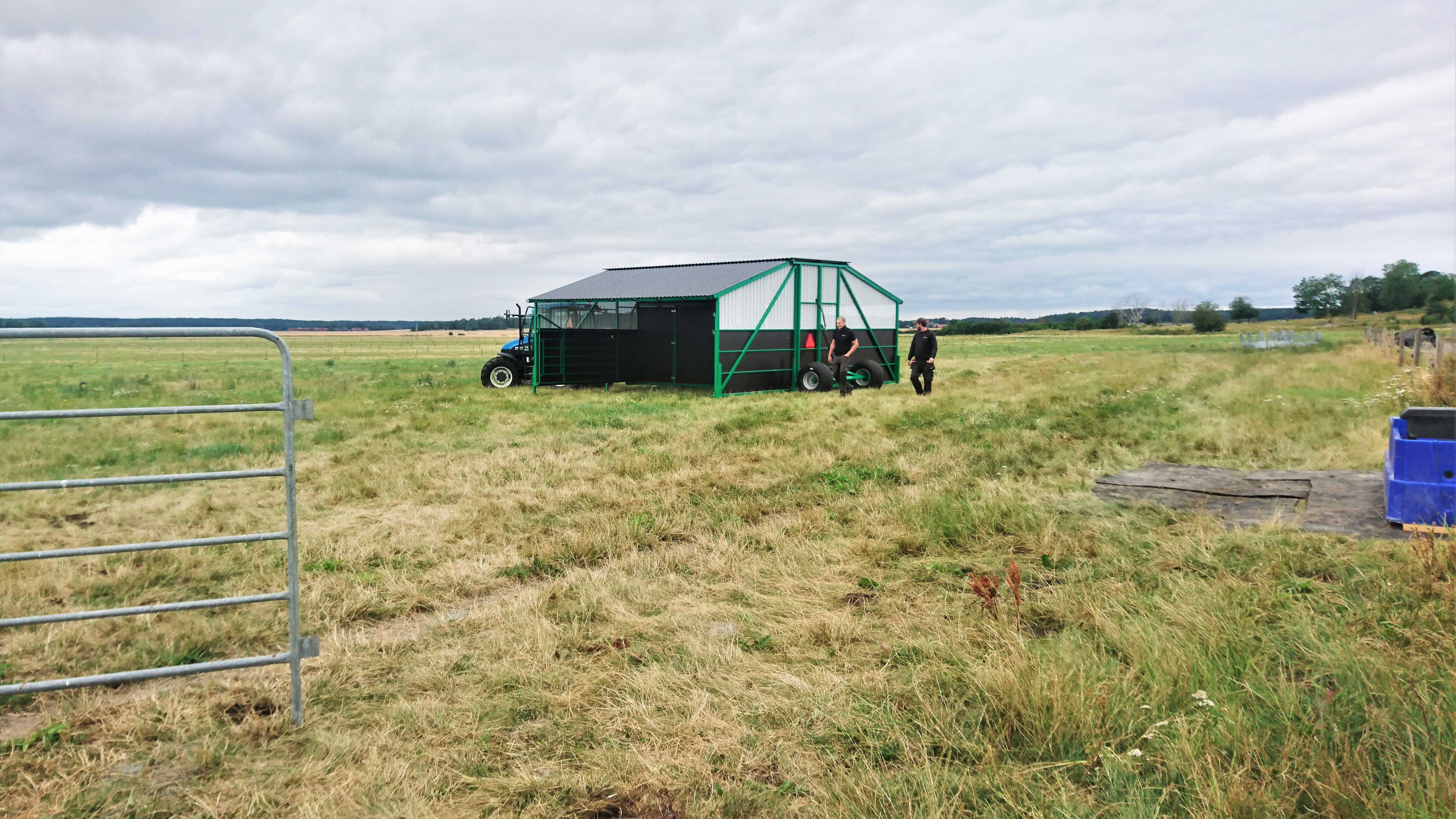 Ett svart och grönt vindskydd som kan flyttas med traktor ute på betet. 