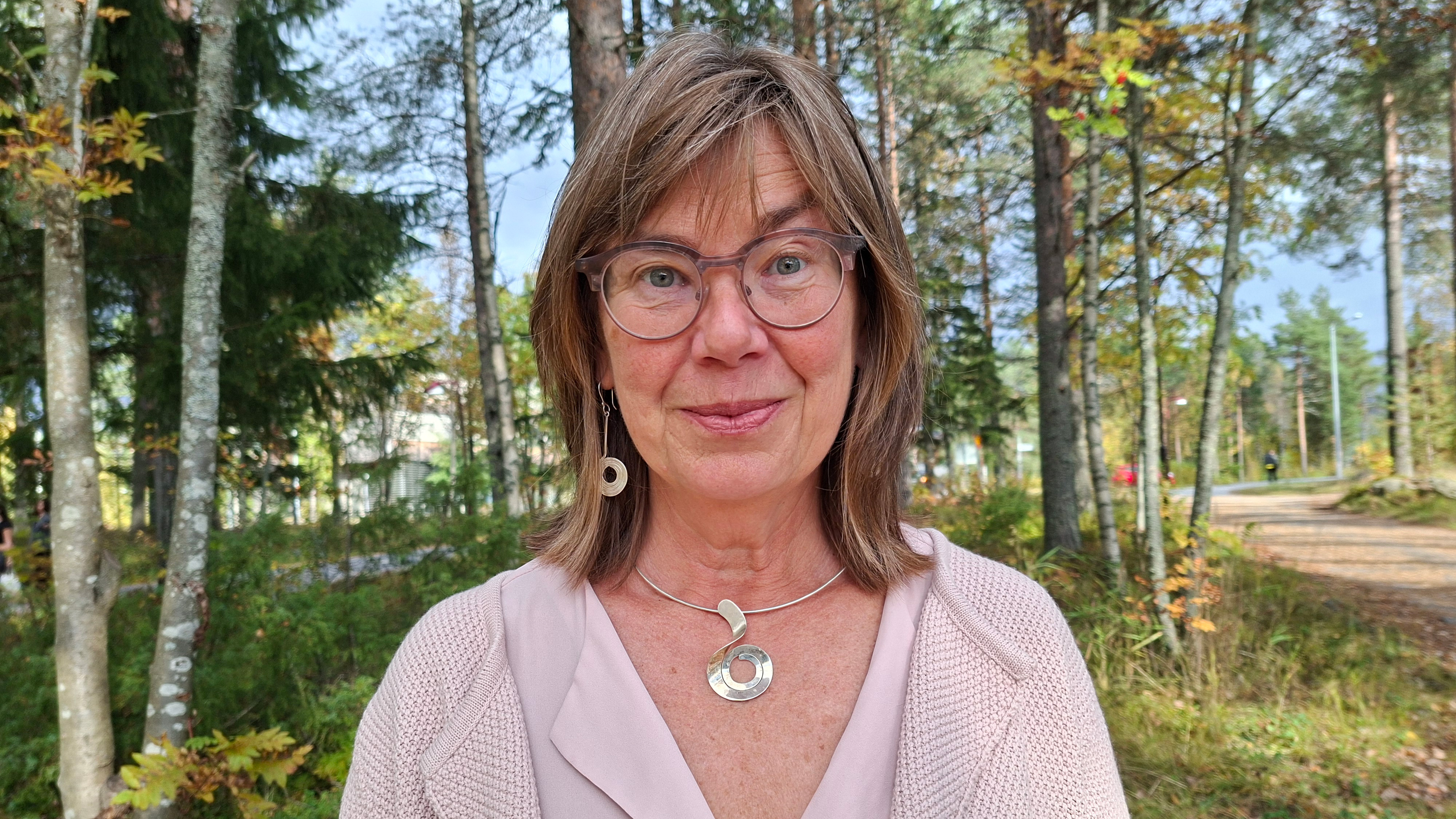 Kvinna i glasögon och stort silvehalsband ler mot kameran.