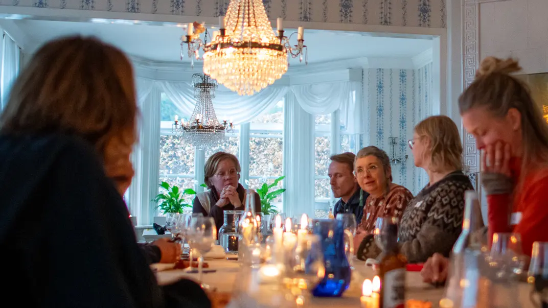 Personer vid ett bord med mat under en kristallkrona. Foto.