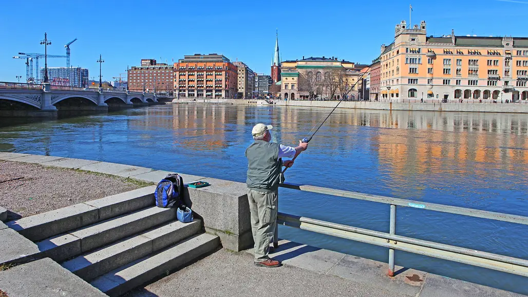 A man fishing in a city canal. Photo.