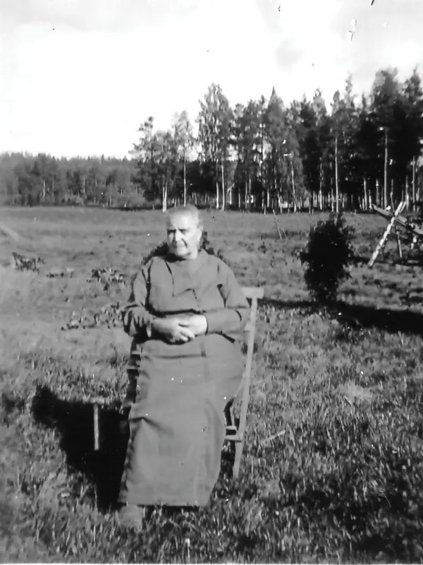 Ett svartvitt foto visar en äldre kvinna som står utomhus. Hon har håret i knut och ser ganska bestämd ut.