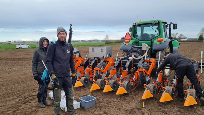 Three people are standing by an agricultural machine.