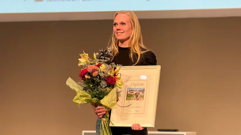 En kvinna med diplom och blombukett. Foto.