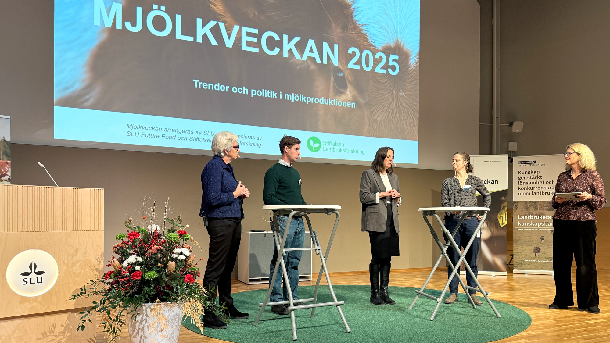 Flera personer vid bord på en scen. Foto.