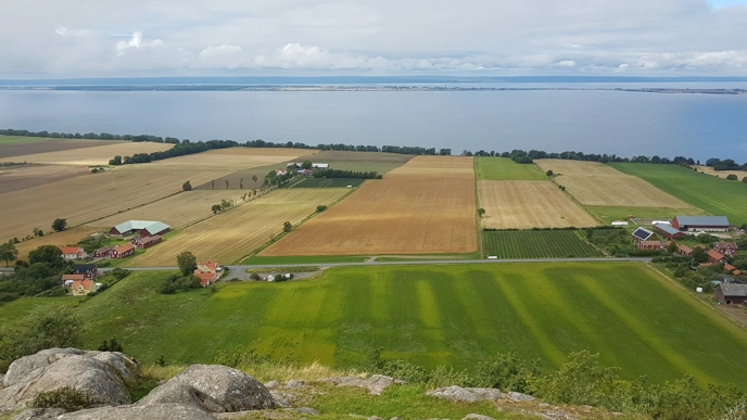 Ett landskap med fält och vatten i bakgrunden.