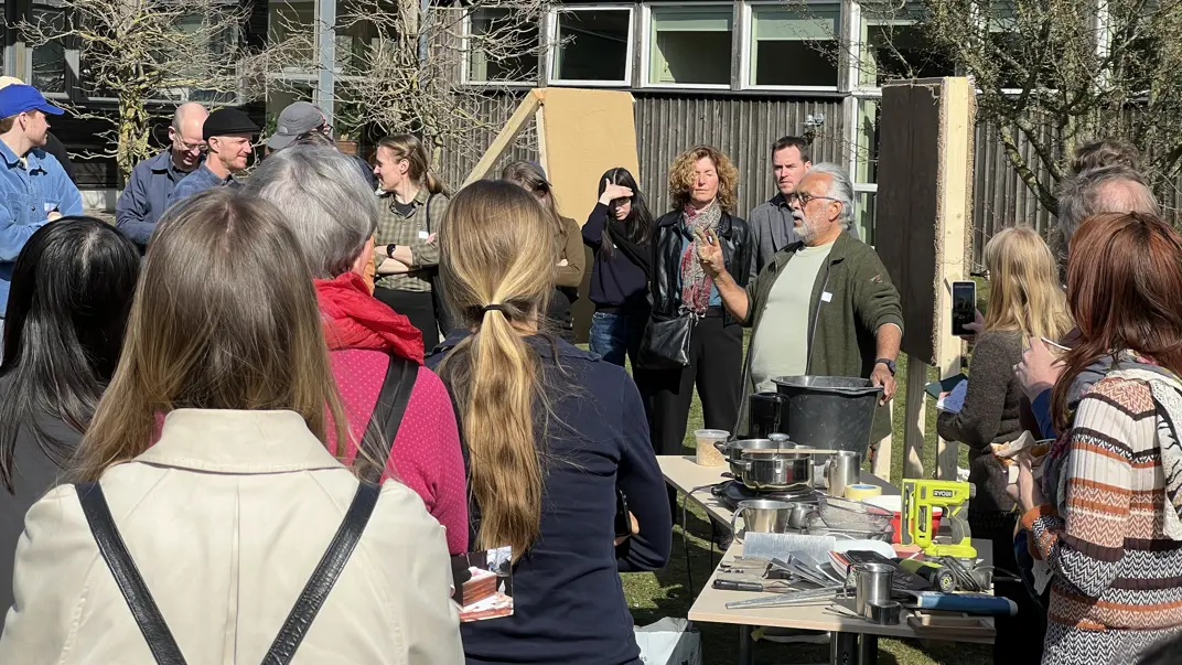 En folksamling iaktar en man som demonstrerar lera som byggmaterial