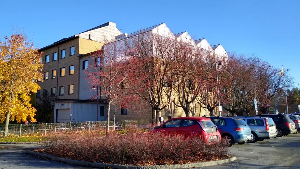 Greenhouse on top of an orange building behind a car park in autumn