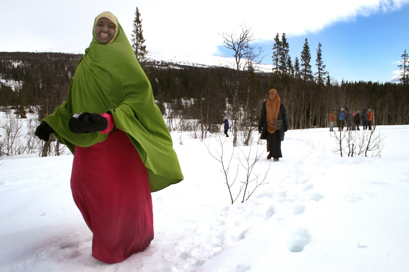Några kvinnor iklädda burkor går leende genom ett snötäckt landskap.