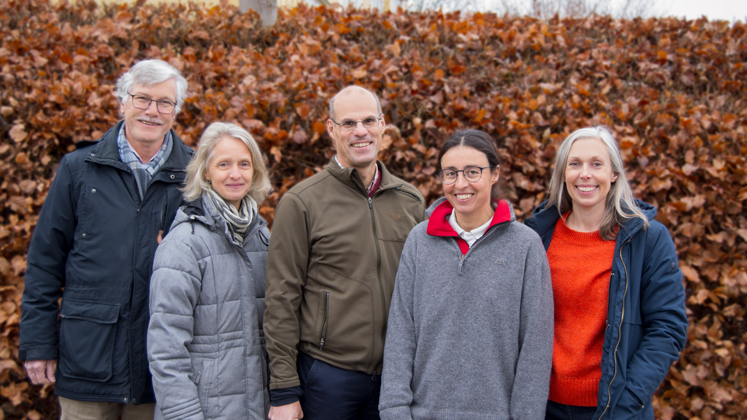 Five persons in front of a shrubbery in autumn colors. Photo.