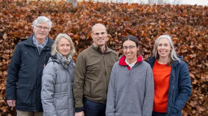 Five persons in front of a shrubbery in autumn colors. Photo.
